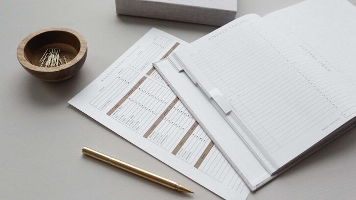 Pages of a journal and client expense sheet with a gold pen on a work desk