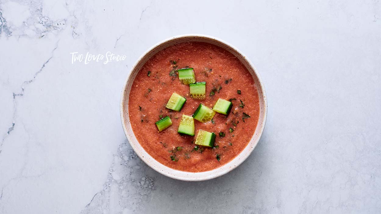 How-to-style soup, gazpacho. A bowl of red soup with cucumber on a marble background.