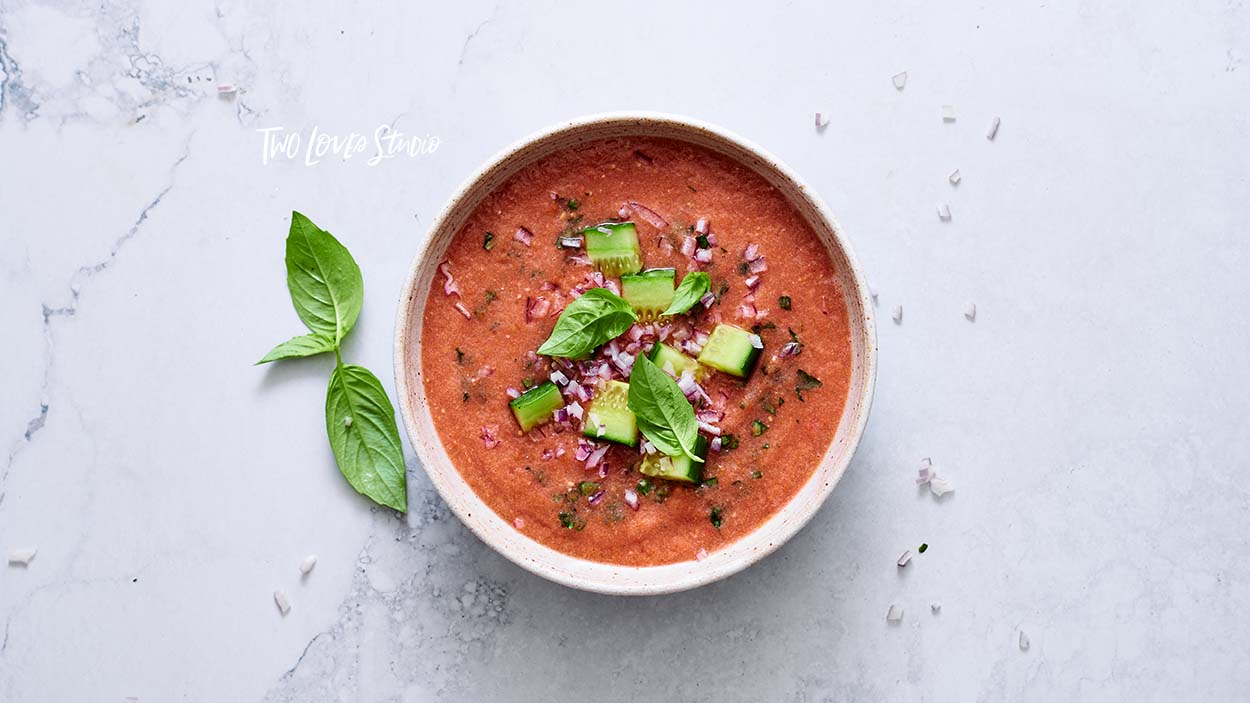 A bowl of gazpacho with toppings on a marble background.